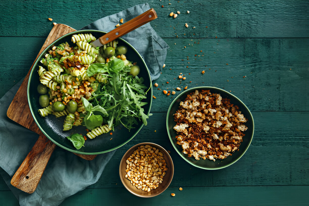 A colorful dish of pasta and greens served in a bowl alongside a small bowl of ingredients.