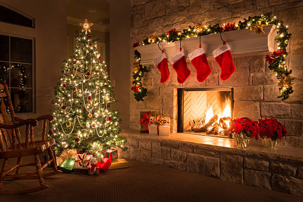 A beautifully decorated Christmas tree beside a stone fireplace adorned with stockings and a warm fire burning.