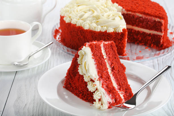 A slice of red velvet cake on a white plate next to a cup of tea.
