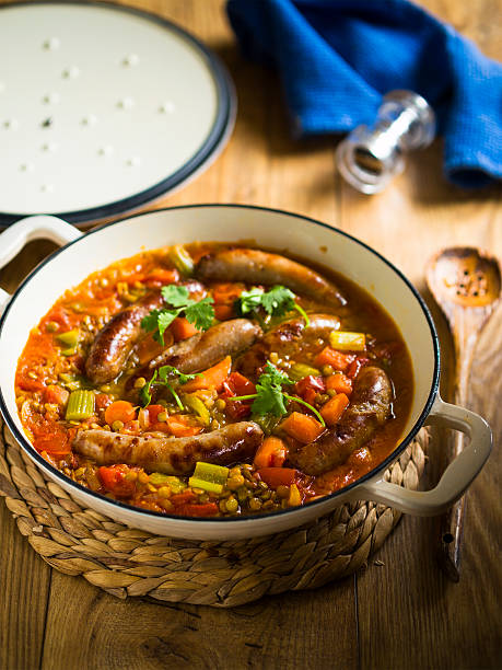 A pot of sausage and vegetable stew garnished with fresh herbs, set on a wooden table.
