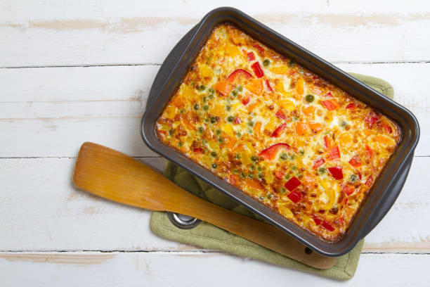 Baked vegetable casserole in a gray pan with a wooden spatula on a green cloth.