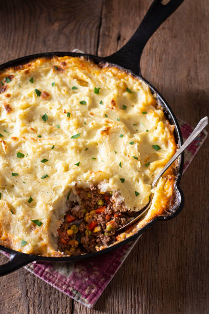 A close-up of a serving of shepherd's pie in a cast iron skillet, showcasing layers of mashed potatoes and a hearty meat filling with vegetables.