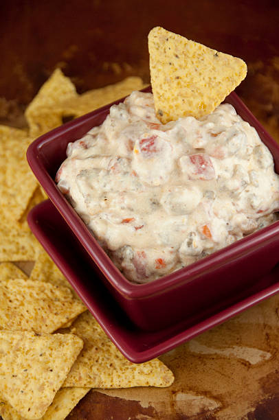 A bowl of creamy dip with a tortilla chip on top, surrounded by scattered tortilla chips.