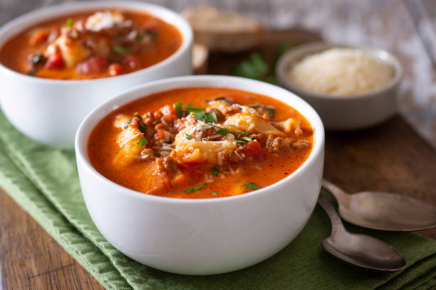Two bowls of creamy tomato soup with pasta and herbs, served on a green napkin.