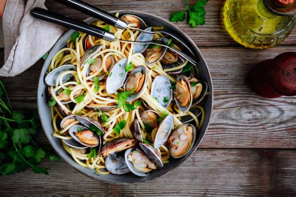 A bowl of spaghetti with clams and fresh herbs on a wooden table.