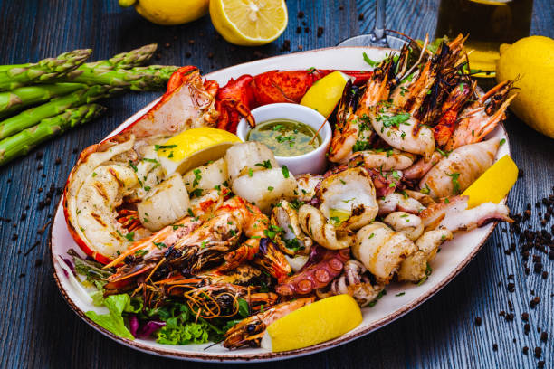 A delicious seafood platter featuring grilled shrimp, lobster, scallops, and squid, garnished with lemon wedges and herbs.