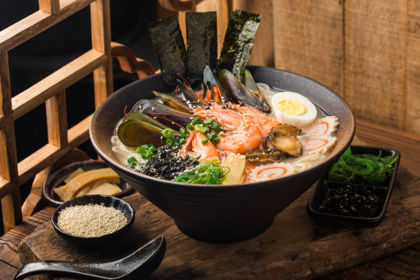 A bowl of ramen topped with shrimp, mussels, and garnished with green onions, seaweed, and sesame seeds.