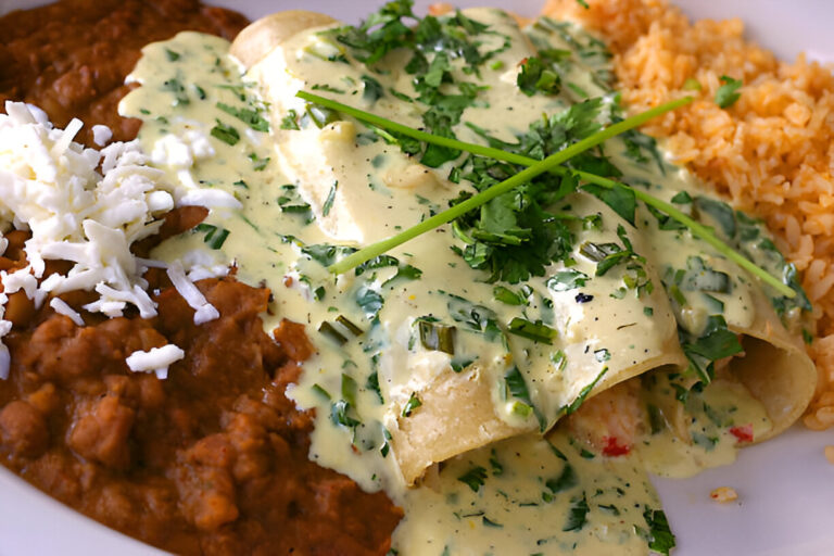A plate of enchiladas topped with creamy green sauce and fresh herbs, served with refried beans and Spanish rice.