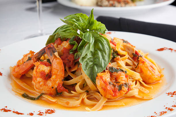 A plate of fettuccine pasta topped with shrimp and fresh basil leaves