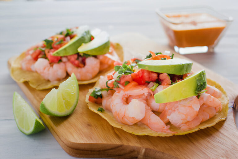 Two shrimp tostadas topped with fresh ingredients on a wooden platter.