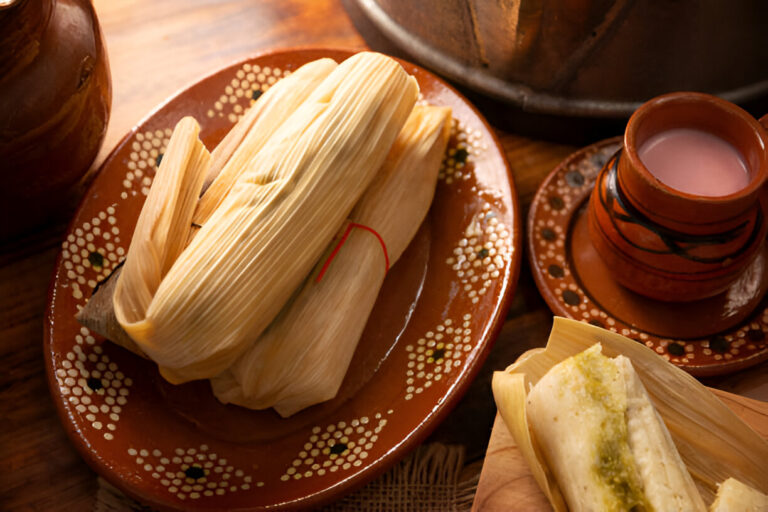 A plate of tamales with a cup of traditional drink on a wooden table.
