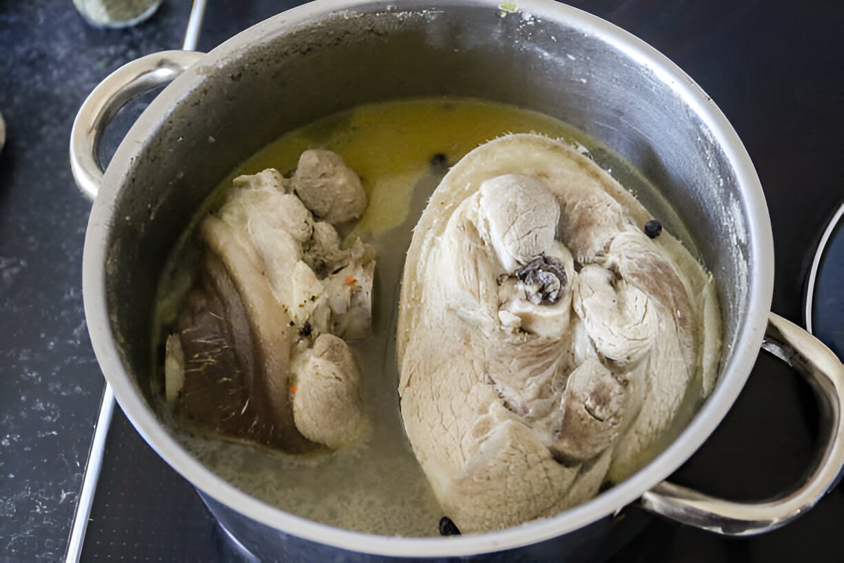 A pot of boiling meat with chunks of bone and fat in a simmering broth.