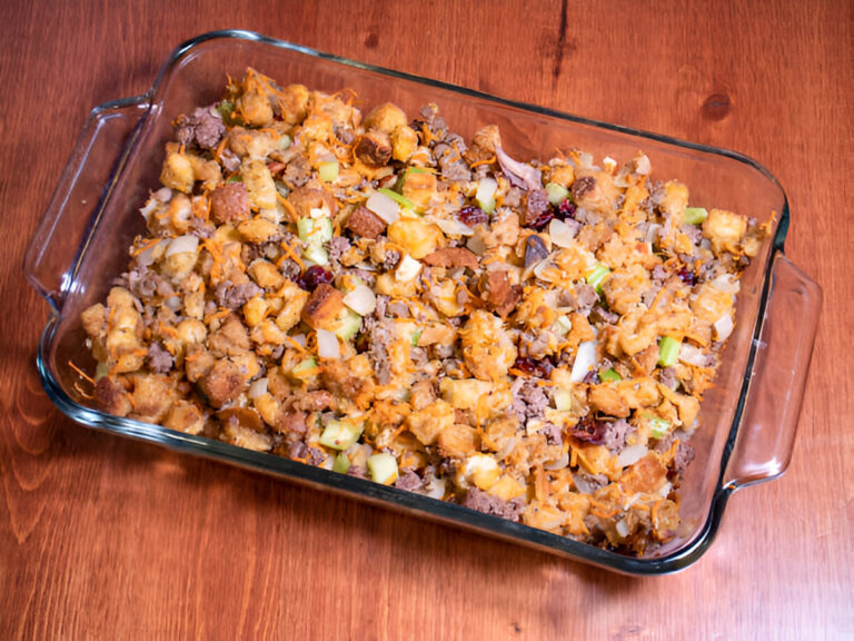 A glass baking dish filled with a savory stuffing mixture containing bread, ground meat, vegetables, and seasonings.