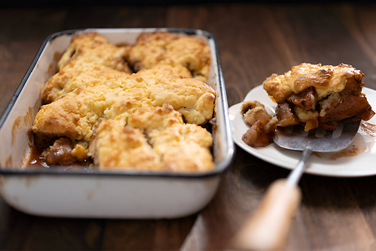 A golden brown cobbler in a baking dish next to a serving on a plate.