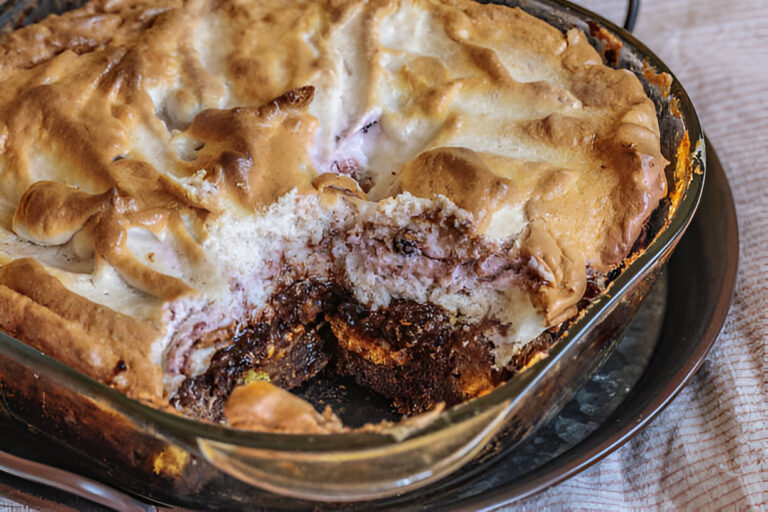 A close-up view of a partially sliced dessert with a golden brown top and visible layers of cream and chocolate.
