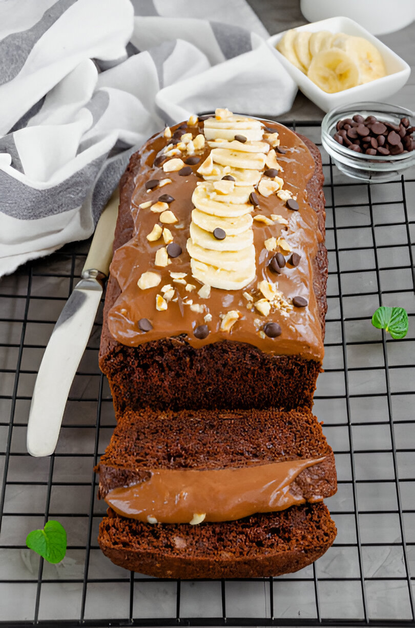 Moist chocolate banana bread topped with sliced bananas, chocolate chips, and chopped nuts.