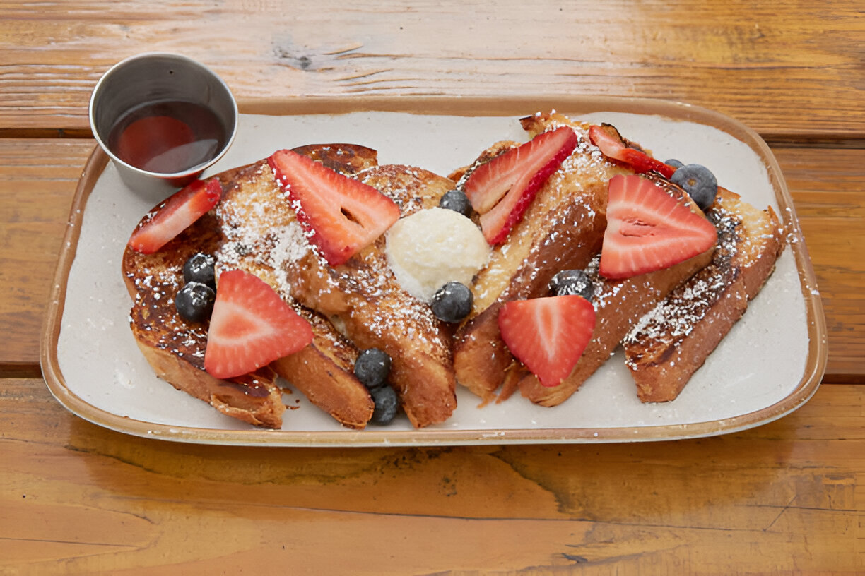 A delicious plate of French toast garnished with fresh strawberries and blueberries, served with a small cup of syrup.
