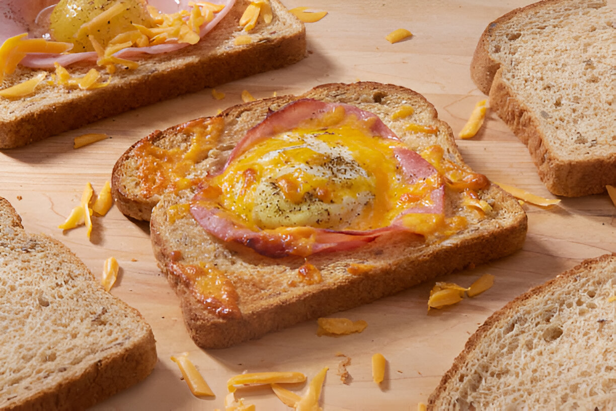 A slice of toasted bread topped with melted cheese, ham, and a sunny-side-up egg.