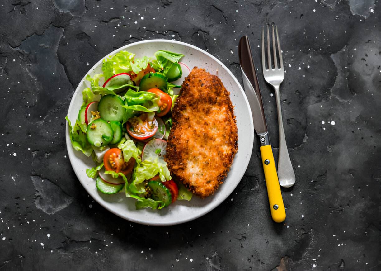 A plate of crispy fried chicken alongside a fresh salad made with lettuce, cucumbers, and cherry tomatoes.