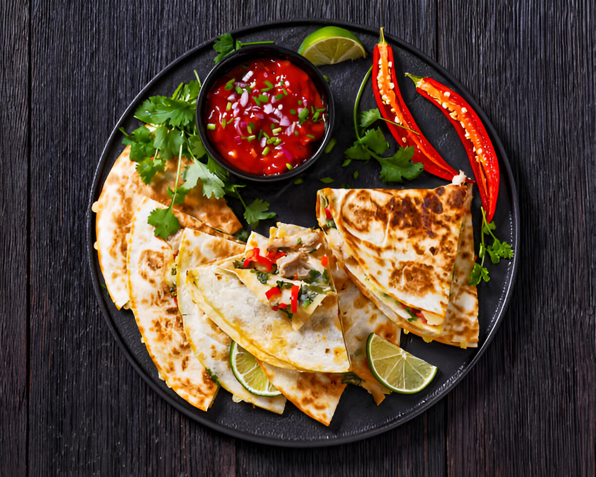 A plate of various quesadillas served with salsa and garnished with fresh herbs and lime.