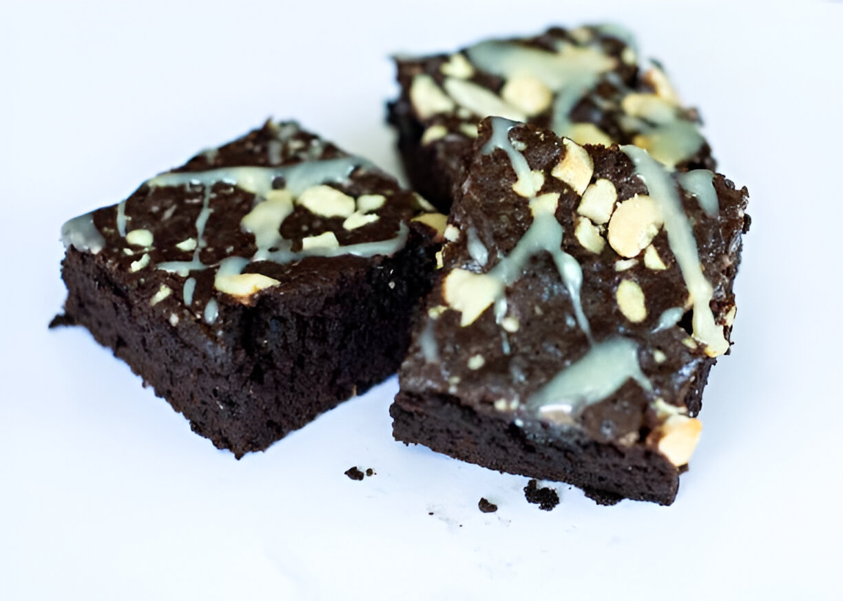 Three chocolate brownies with a light drizzle and chopped nuts on top, served on a white plate.