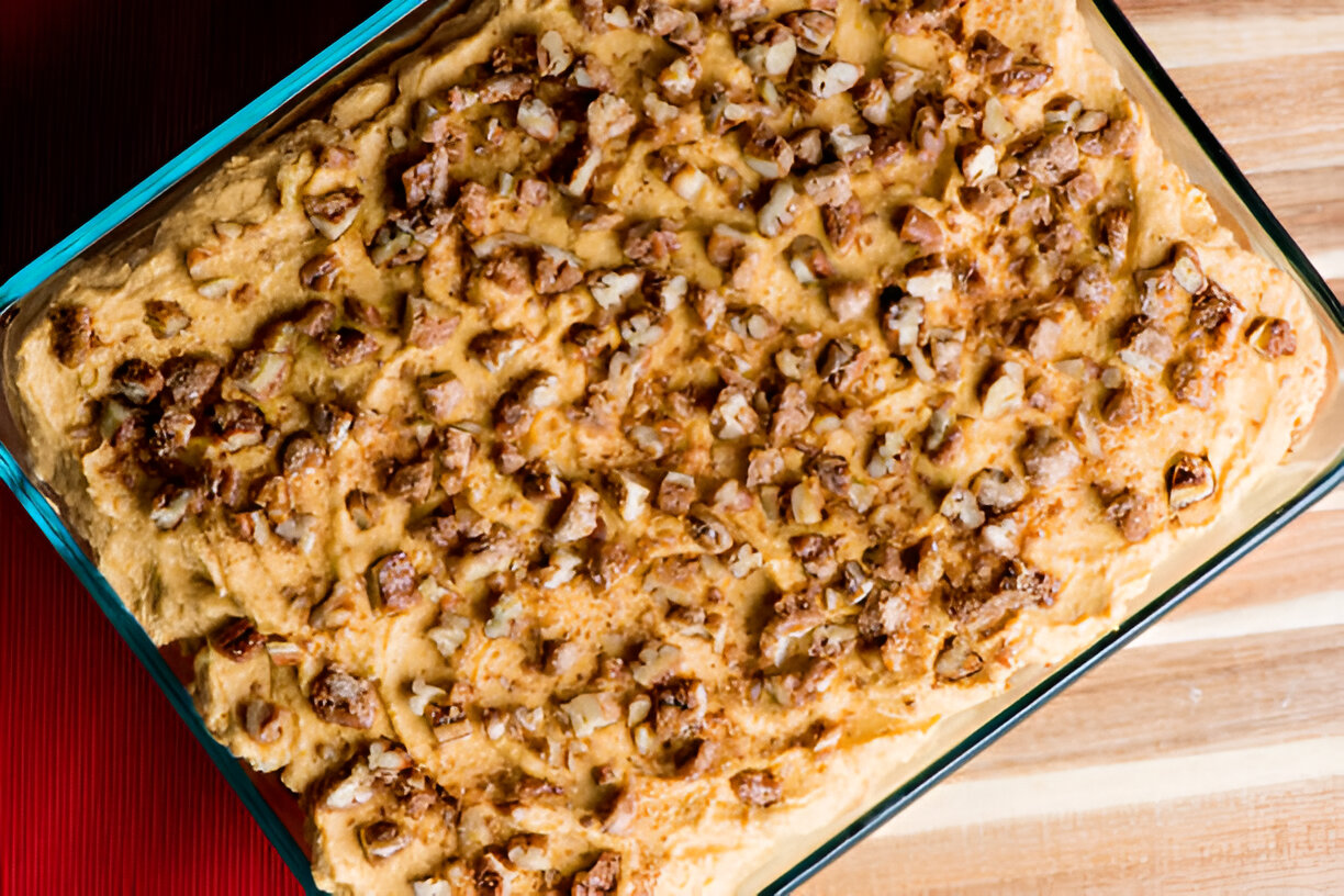 Baked dish topped with finely chopped nuts in a glass baking dish on a wooden surface.