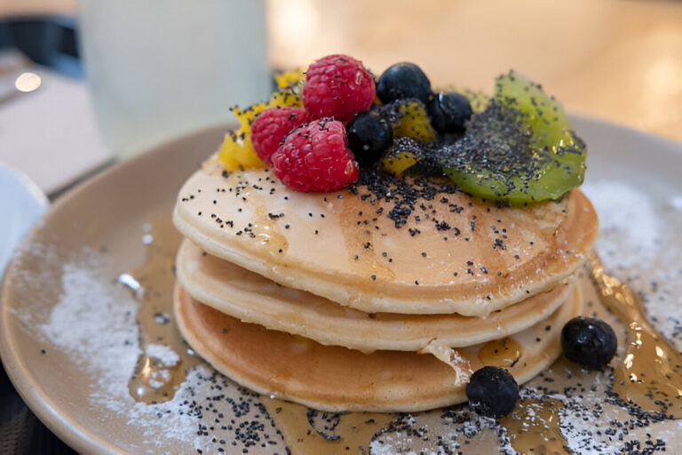 Stack of pancakes topped with fruits and syrup