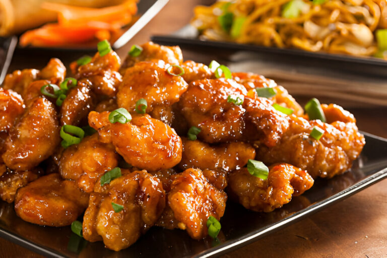 A close-up view of a plate of glazed chicken pieces garnished with chopped green onions.