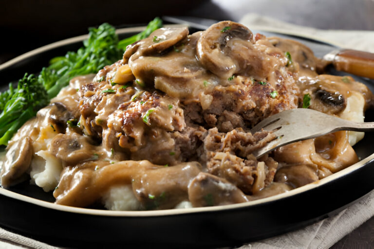 A plate of meatloaf topped with mushroom gravy served with mashed potatoes and broccolini.