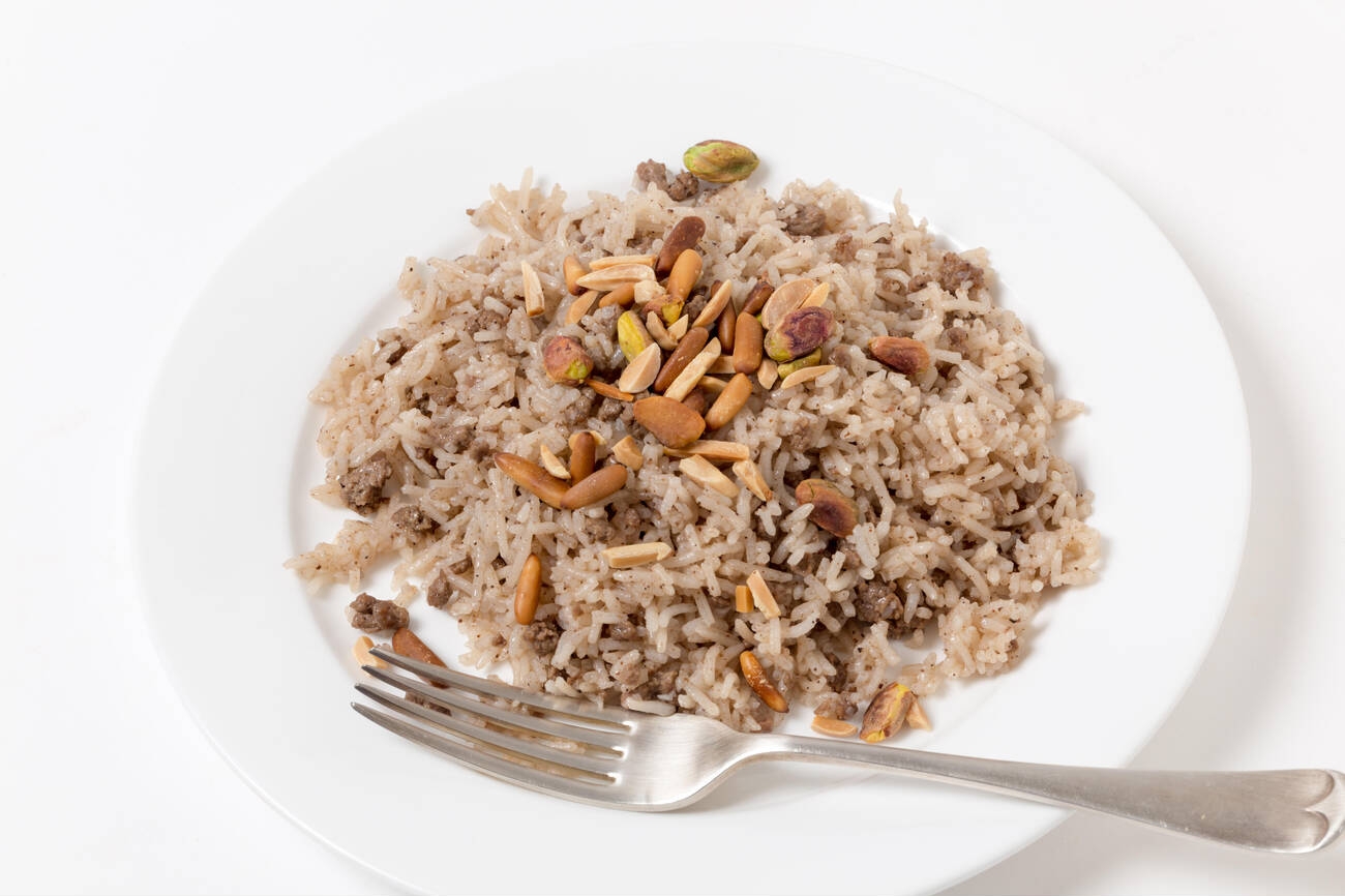 A plate of rice dish topped with nuts, served with a fork