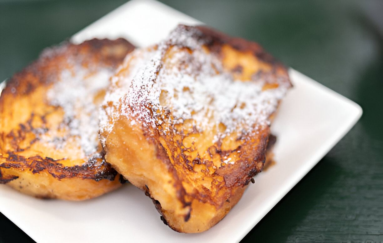 Two pieces of French toast dusted with powdered sugar on a white plate