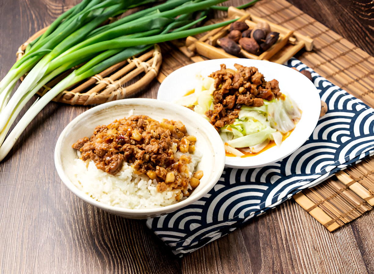A comforting meal consisting of rice topped with savory meat sauce and a side of sautéed cabbage, surrounded by fresh green onions.