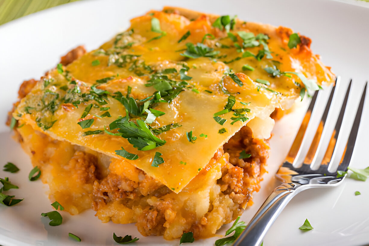 A slice of hearty casserole topped with melted cheese and fresh chopped herbs on a white plate.