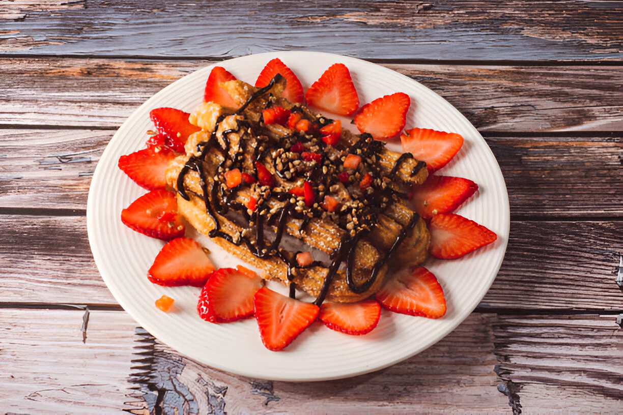 A plate of dessert featuring churros topped with chocolate sauce and fresh strawberries.