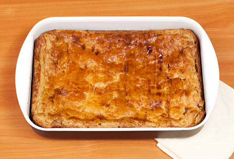 A freshly baked pastry in a white baking dish on a wooden table.