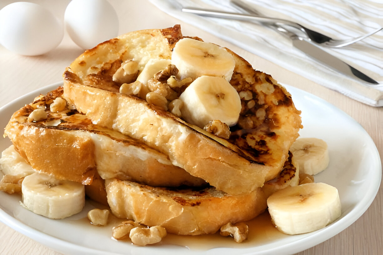Plate of French toast topped with banana slices and walnuts, with eggs in the background.