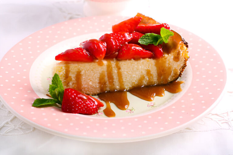 A slice of cheesecake topped with fresh strawberries and caramel sauce on a polka dot plate.