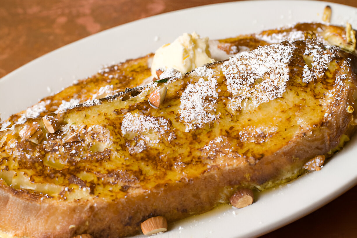 A delicious plate of French toast topped with powdered sugar and almond slices, served with a dollop of butter.