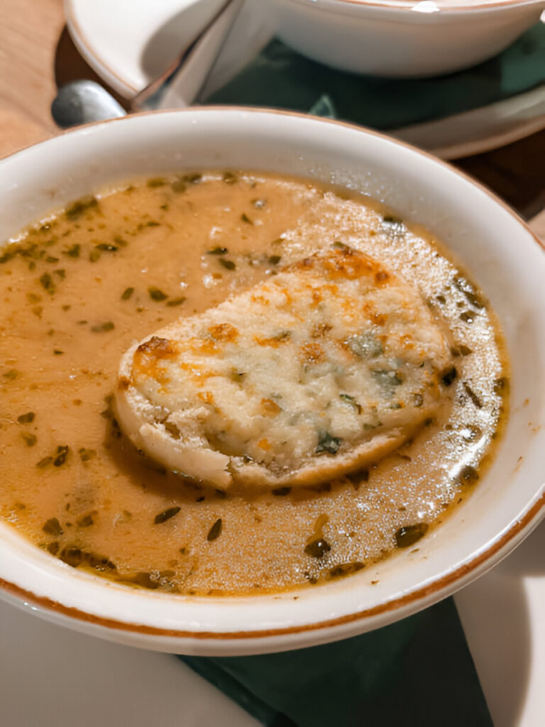 A bowl of soup with a slice of toasted bread on top, garnished with herbs.