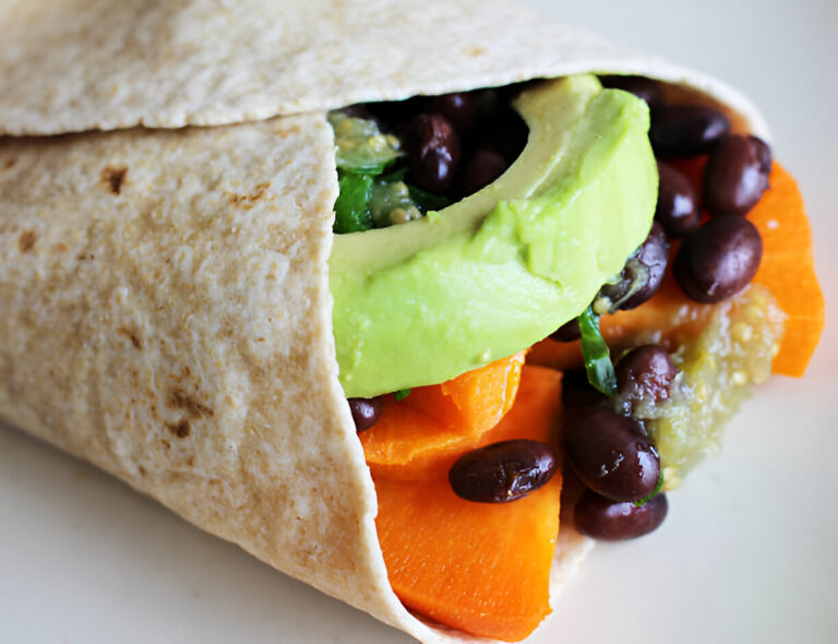 Close-up of a whole wheat wrap filled with beans, avocado, and orange carrots.