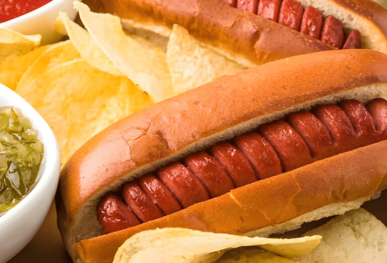Two hot dogs served in buns, accompanied by potato chips and pickles.