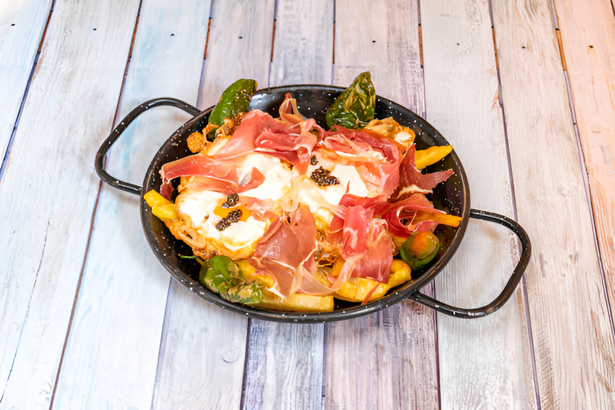 A colorful dish featuring eggs, prosciutto, and vegetables in a black frying pan.
