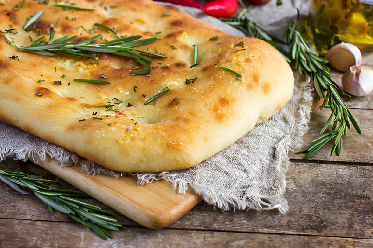 Freshly baked focaccia bread topped with rosemary on a wooden board.