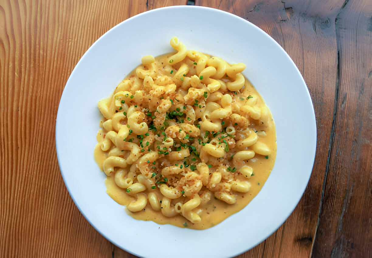 A creamy macaroni dish topped with green herbs and crispy breadcrumbs, served in a white bowl on a wooden table