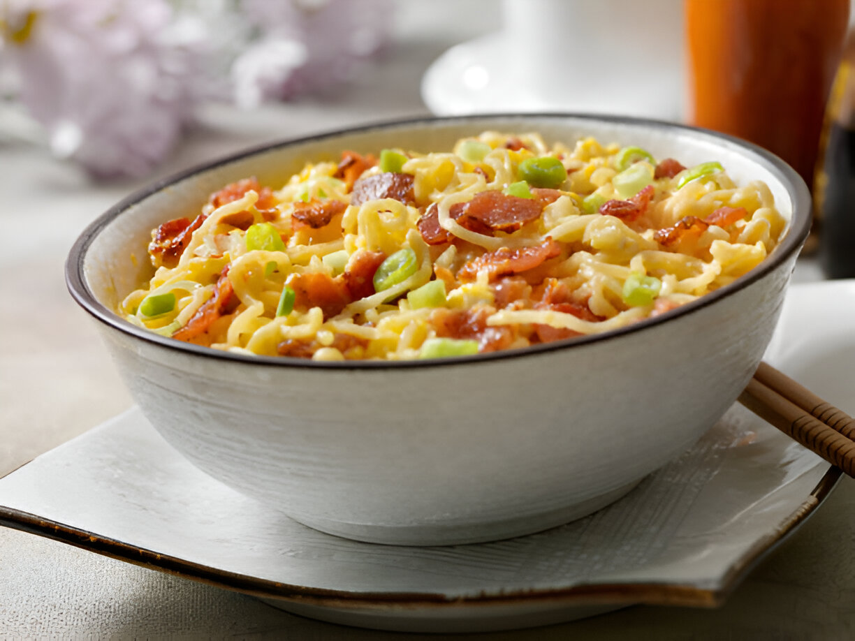 A bowl of noodles topped with green onions and crispy bacon.