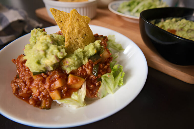 A plate of nachos topped with guacamole, lettuce, and a garnish of tortilla chip.