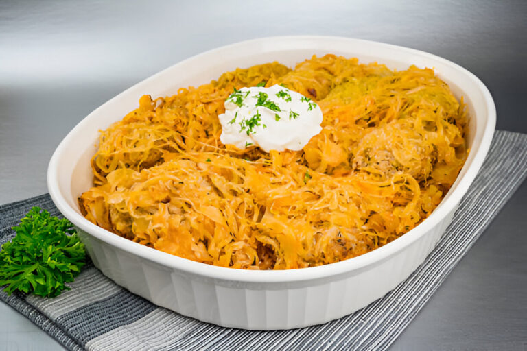 A baked dish with a golden topping, featuring shredded ingredients and a dollop of sour cream on top, garnished with chopped herbs.