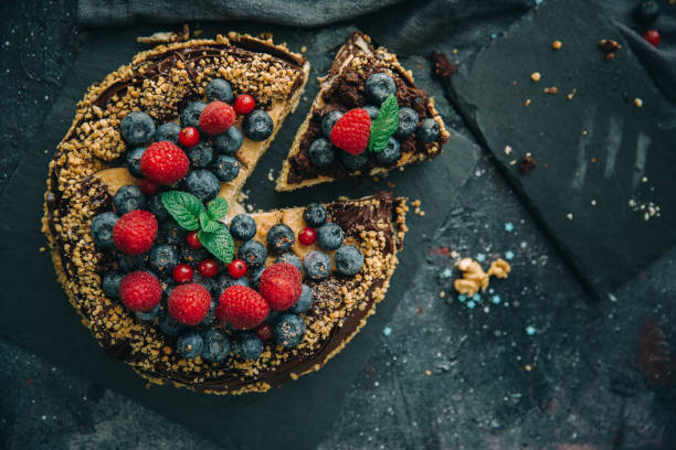 A delicious cake topped with fresh berries, including raspberries and blueberries, garnished with mint leaves, on a dark surface.