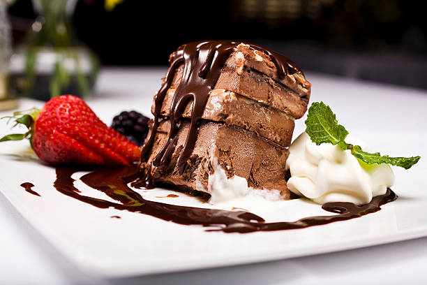 A decadent chocolate dessert served on a white plate with whipped cream, strawberries, and a drizzle of chocolate sauce.