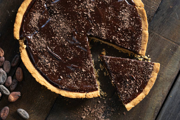 A delicious chocolate tart on a wooden table, with one slice removed and cocoa powder sprinkled on top.